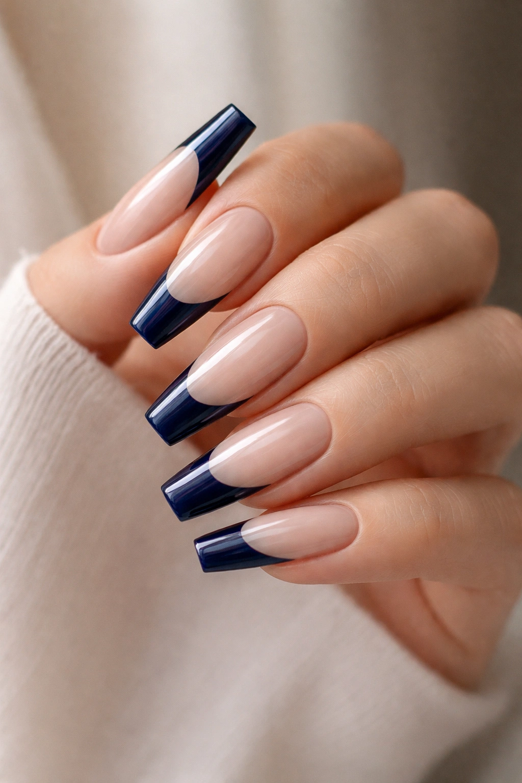 Close-up of navy blue coffin nails with glossy French tips on a hand