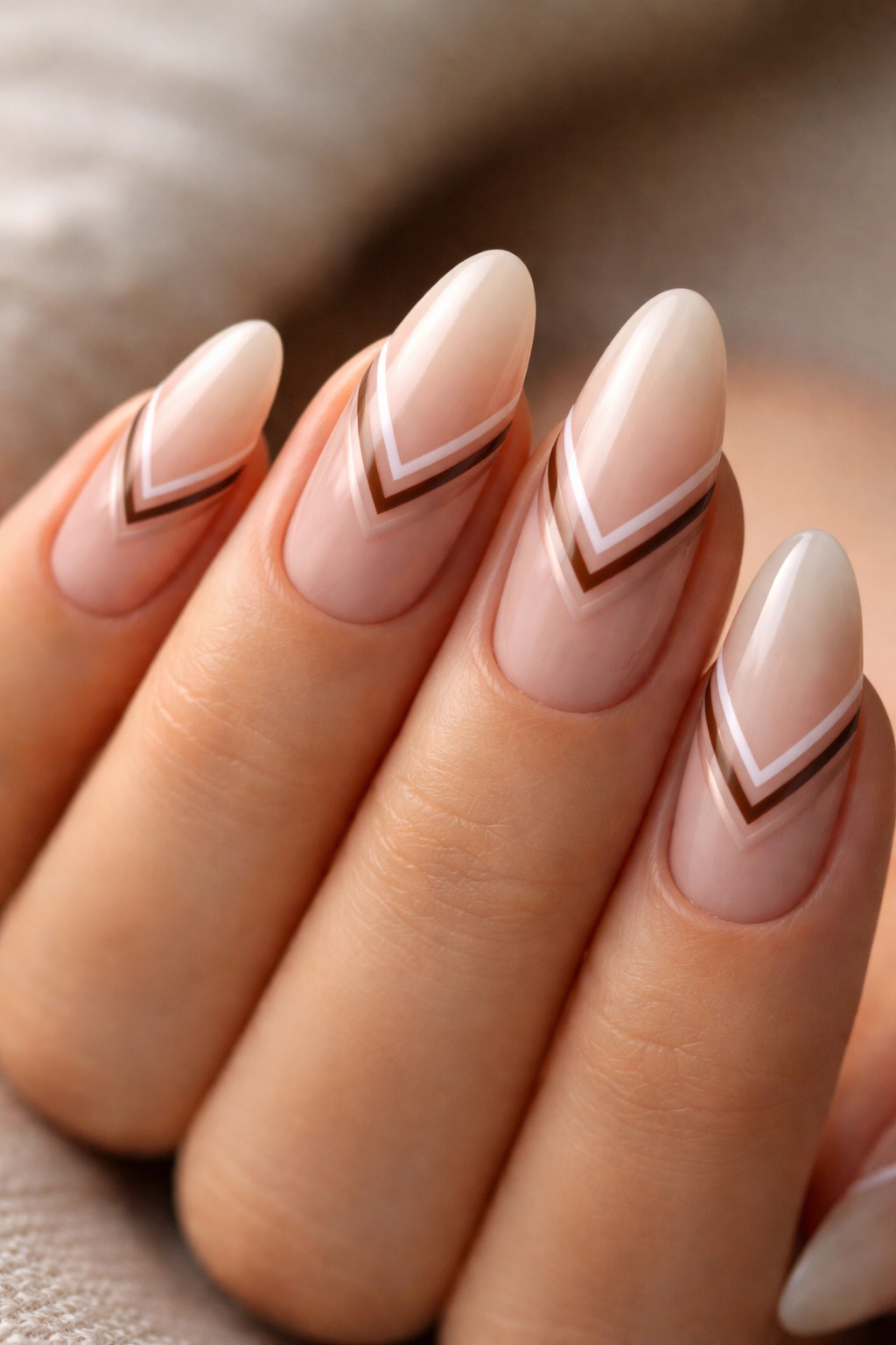Nude almond nails with a slim negative-space chevron near the cuticle