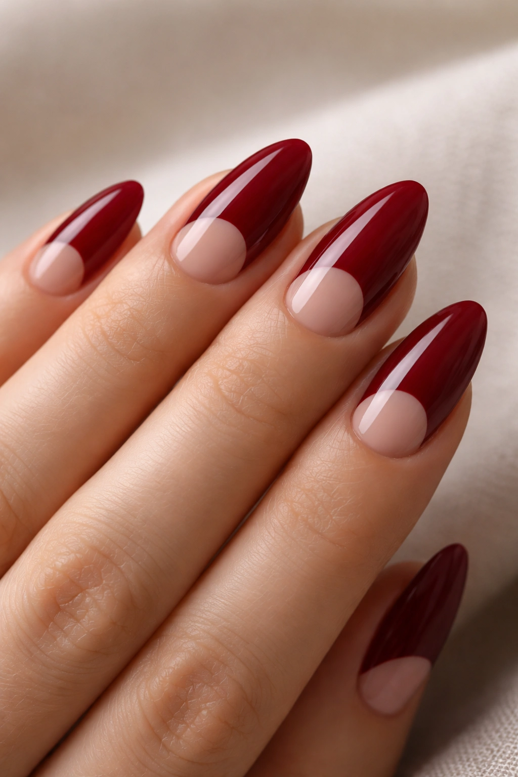 Almond nails showing negative-space half moon design in deep red polish