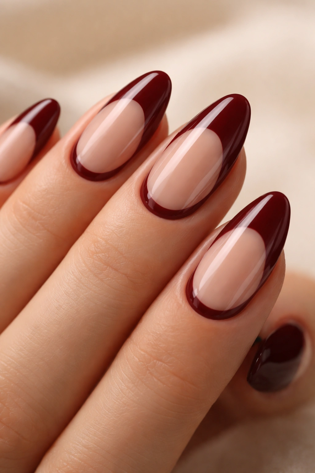 Close-up of almond nails with maroon negative-space cuticle art on a neutral background