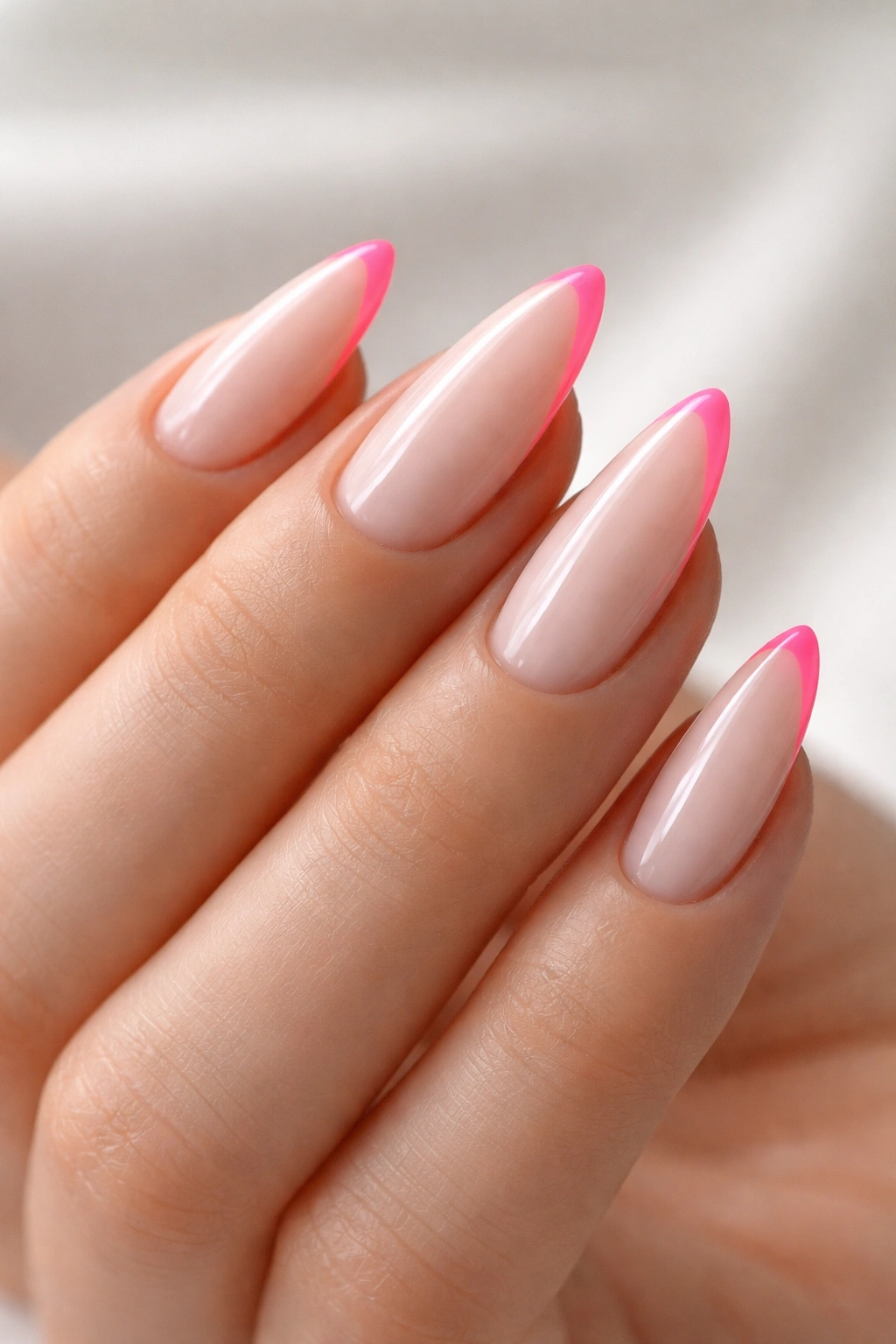 Close-up of almond nails with thin neon pink tips on a milky base