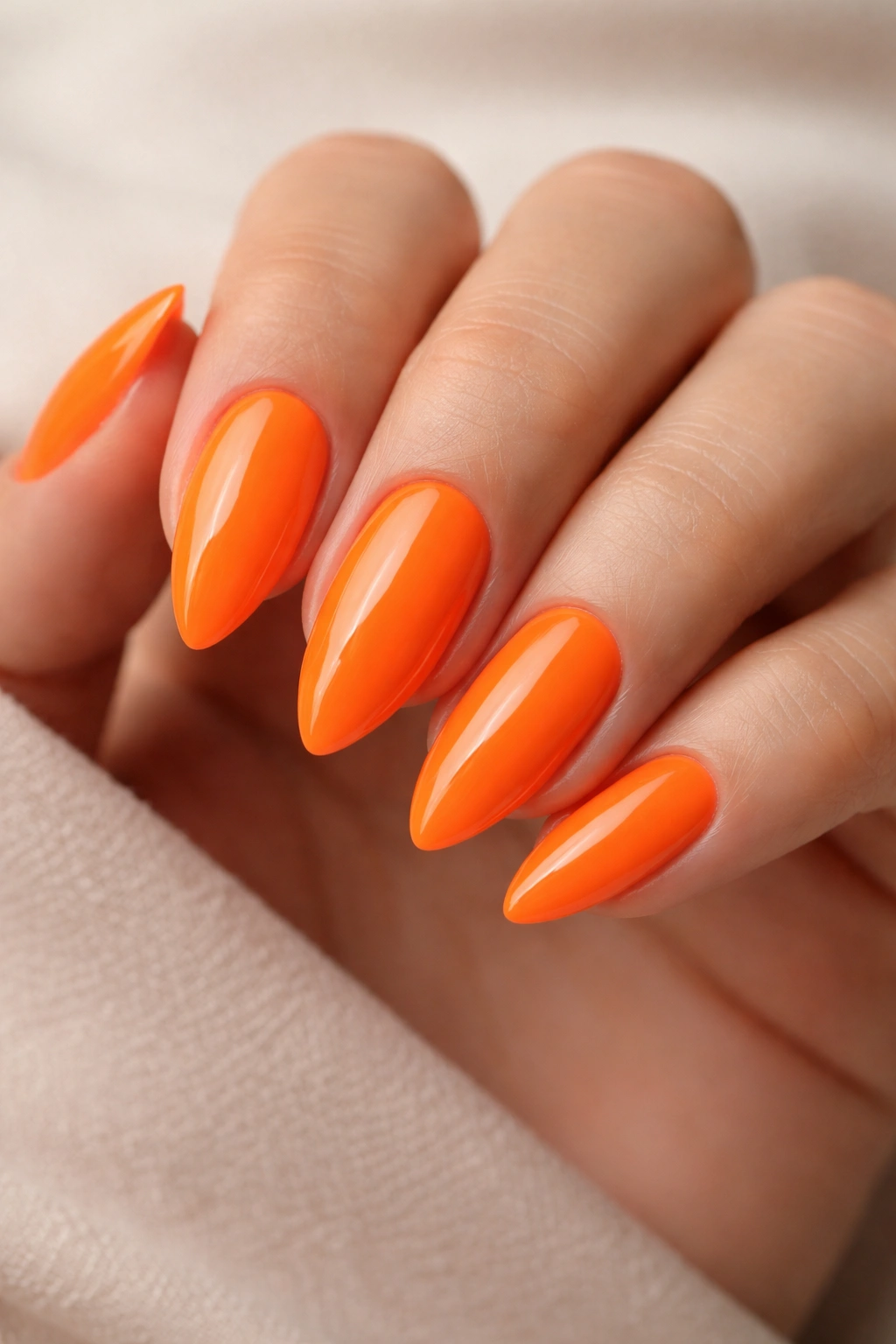 Close-up of neon tangerine almond nails with a vivid orange color