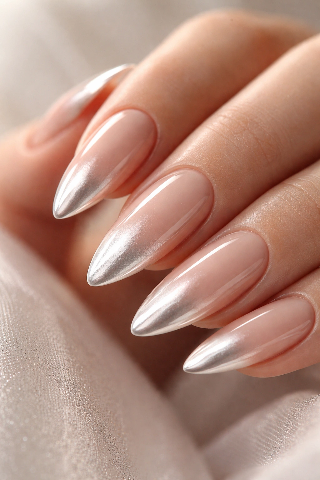 Close-up of nude to chrome ombre almonds nails with reflective tip