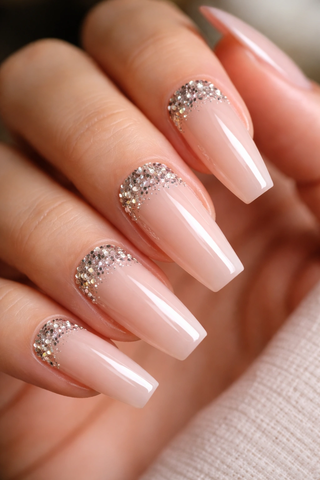Nude coffin nails with chunky glitter at the cuticle crescent