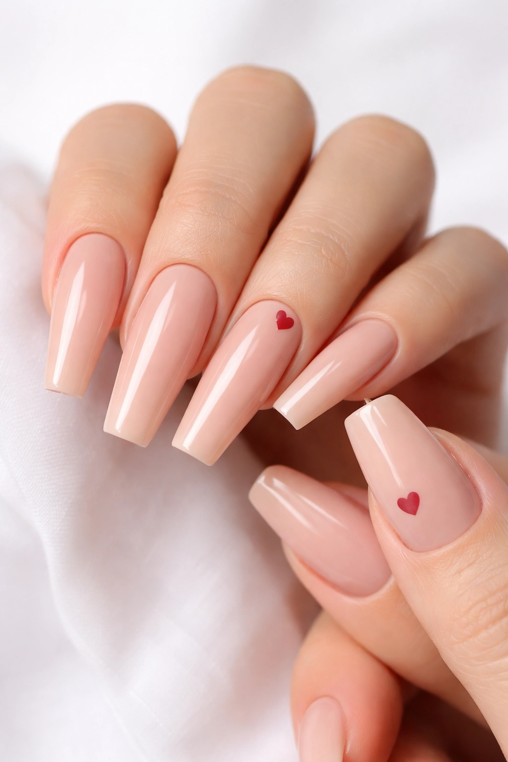 Close-up of nude coffin nails with tiny heart accents on two nails