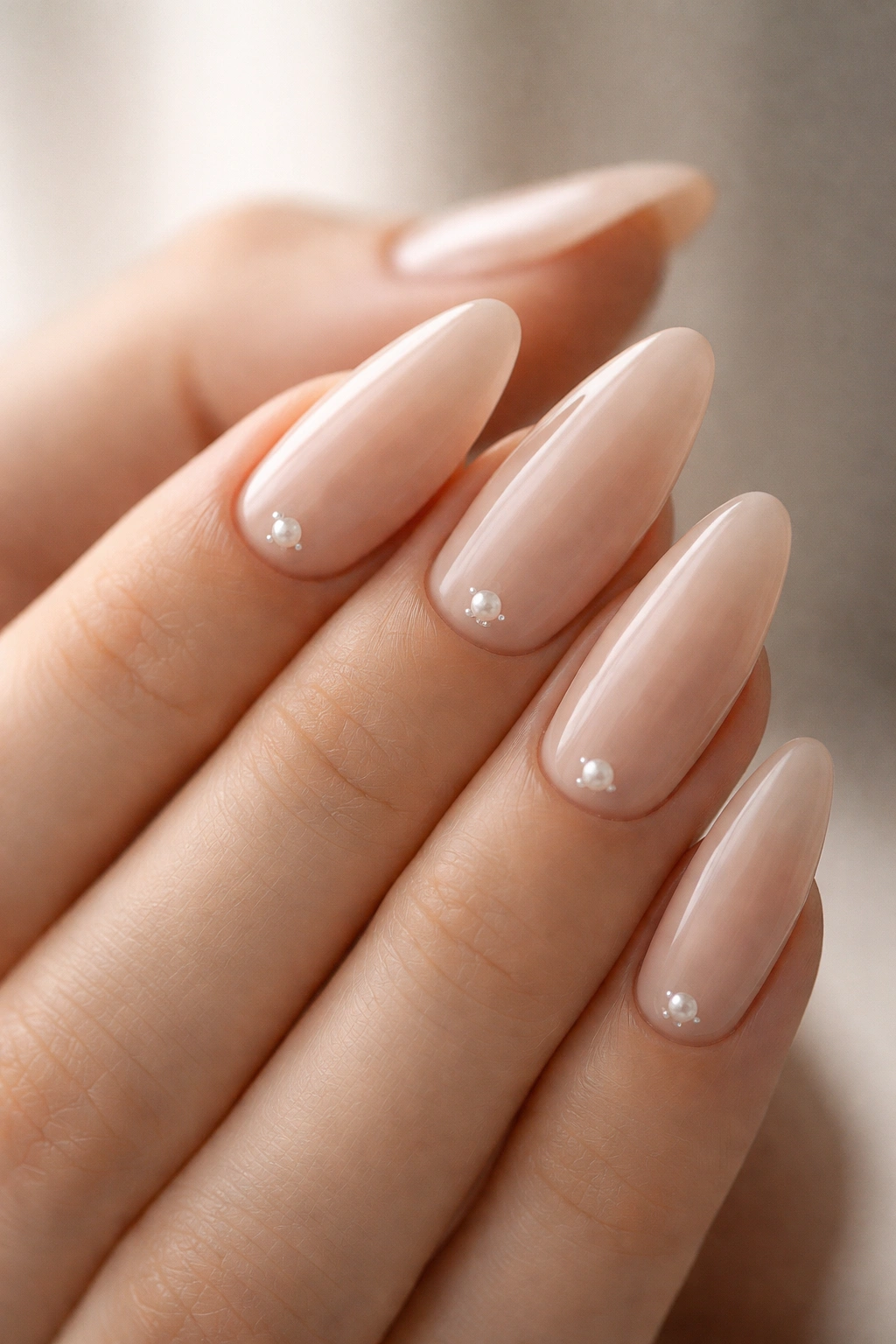 Close-up of nude almond nails with tiny pearl dot accents by the cuticle