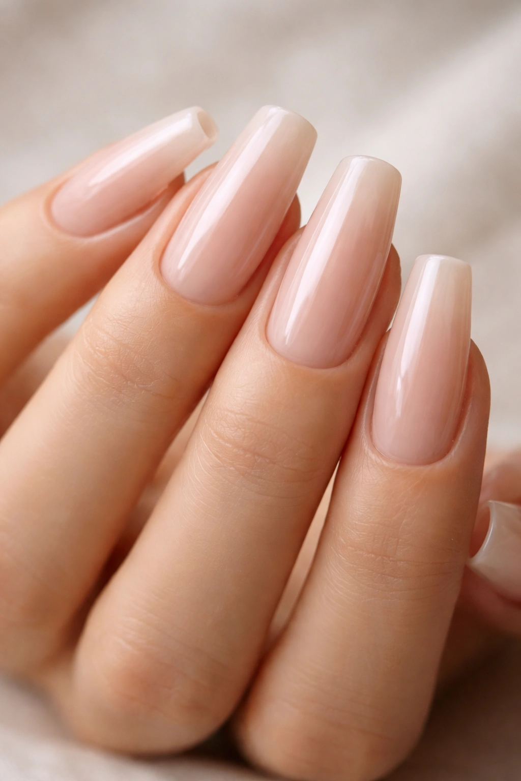 Close-up of soap-nail nude ballerina nails with glossy semi-sheer pink-beige finish