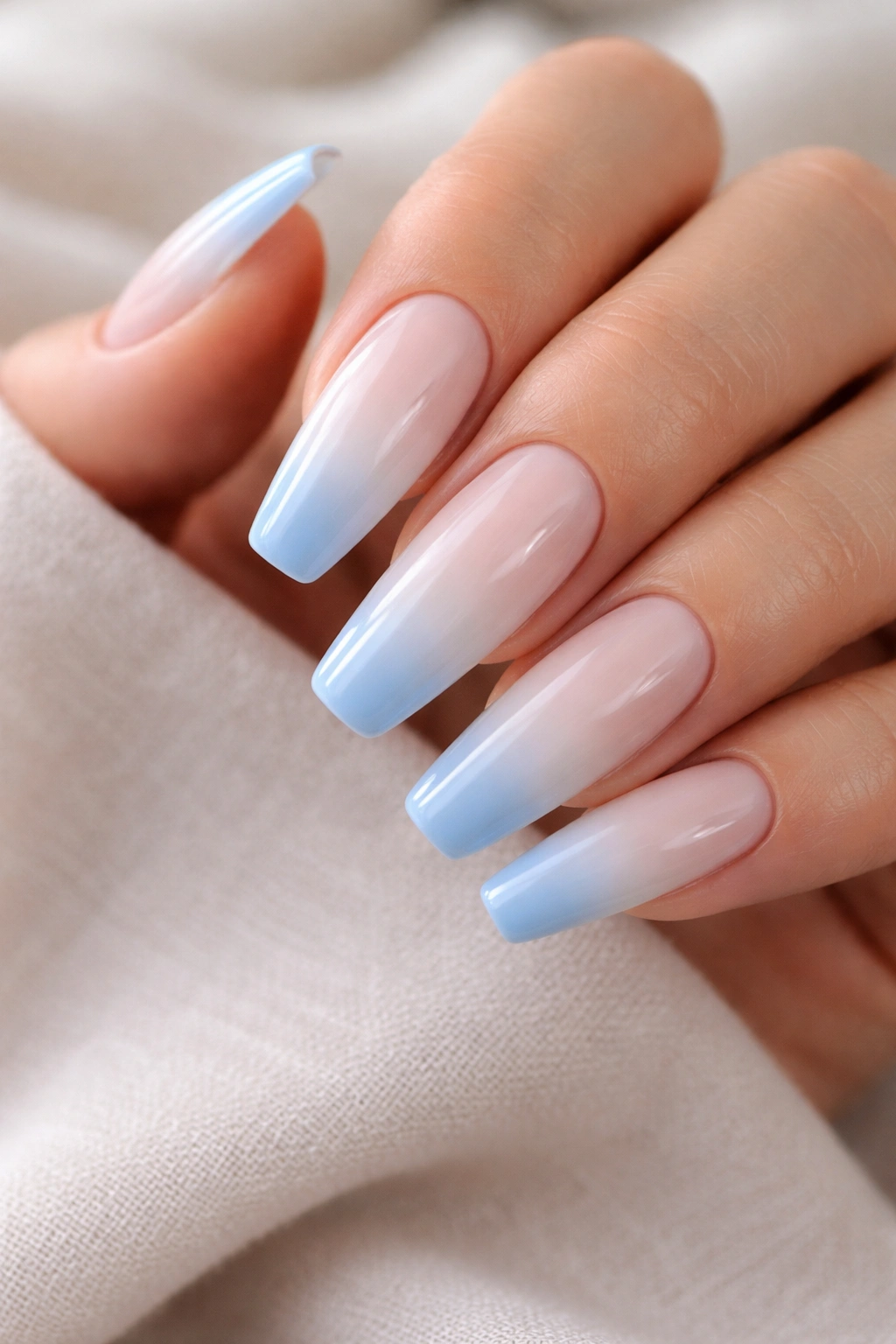Close-up of long coffin nails with milky base and light blue ombre tips.