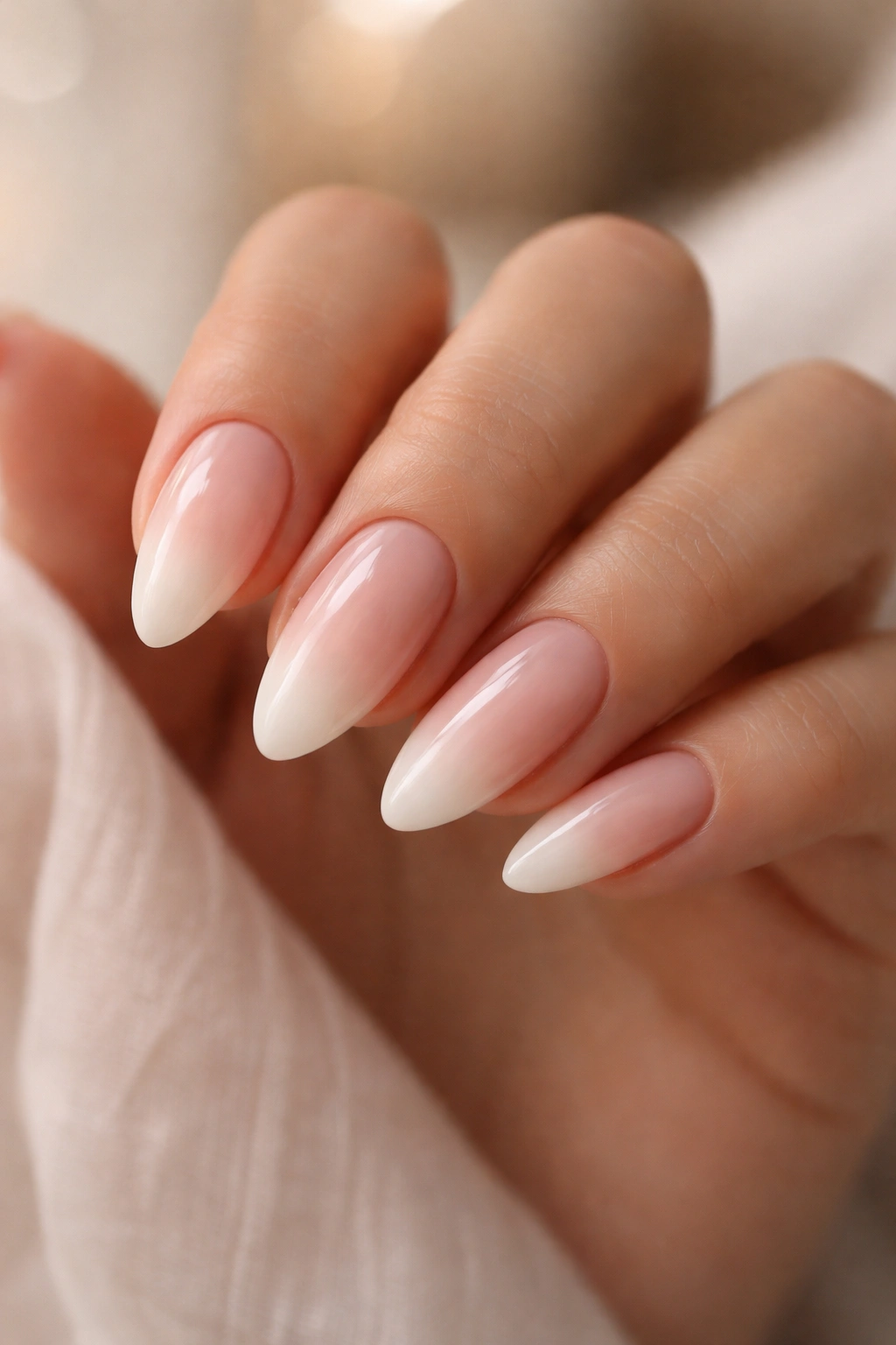 Close-up of ombré almond nails with a seamless blush to white gradient.