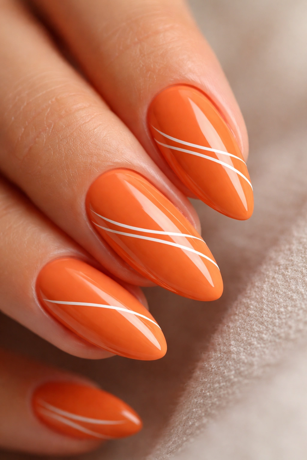 Close-up of orange almond nail with white line art on a bare finger