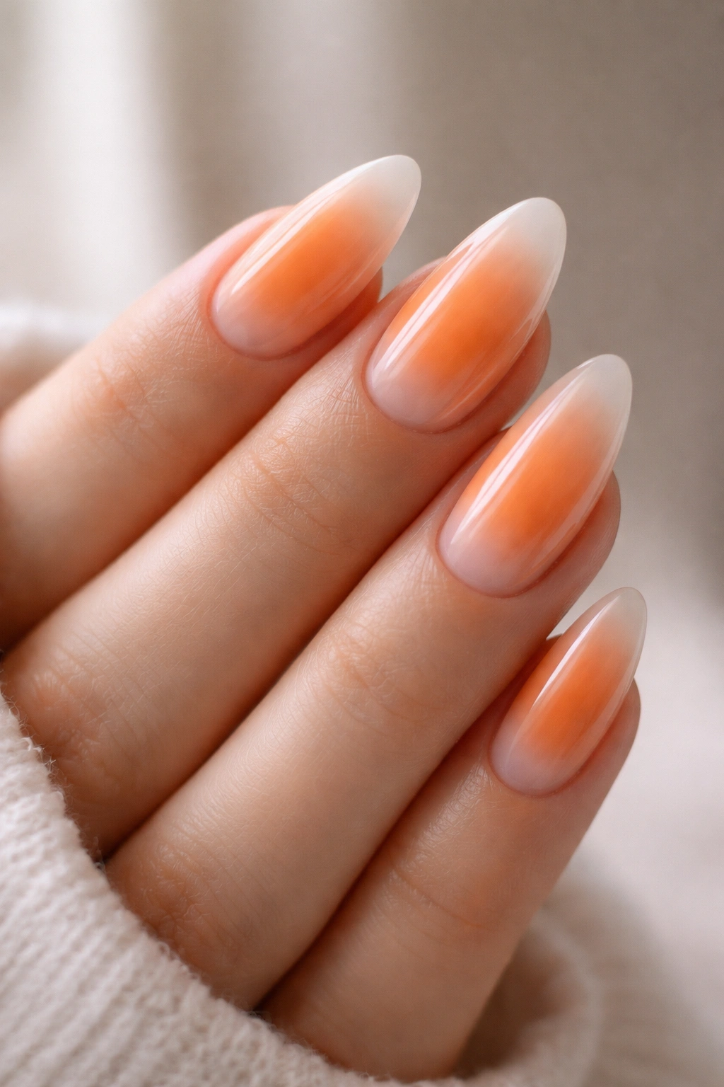 Close-up of orange aura almond nails showing a soft orange center fading to milky edges