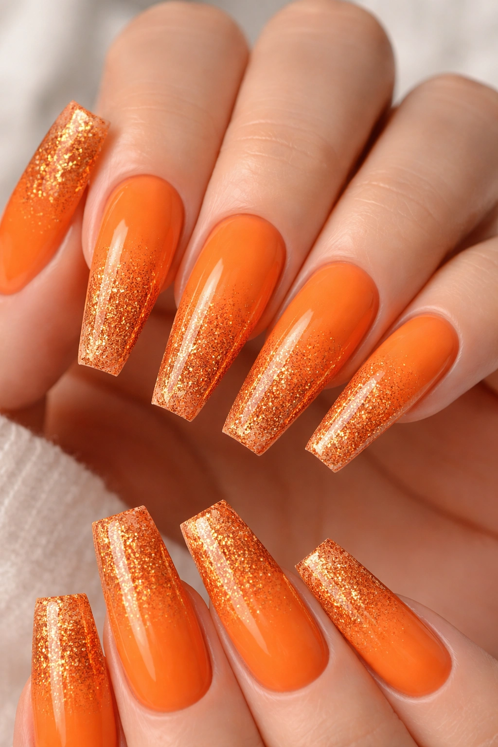 Close-up of orange coffin nails with a glitter fade toward the tip