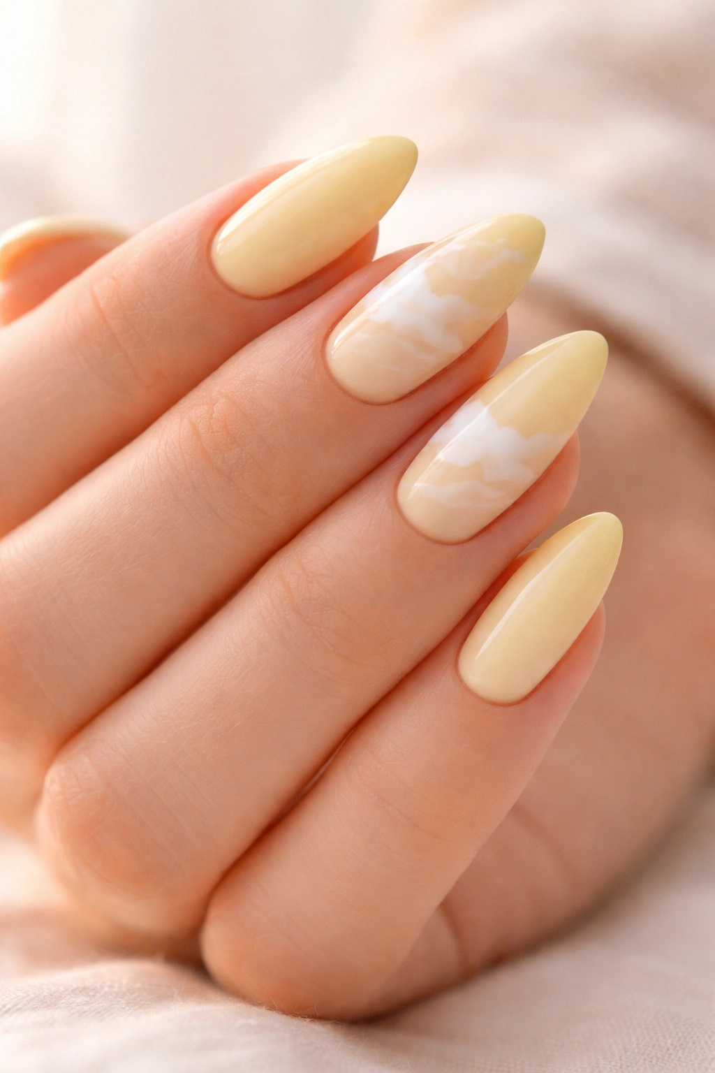 Pale canary nails with white cloud swirls on almond nails