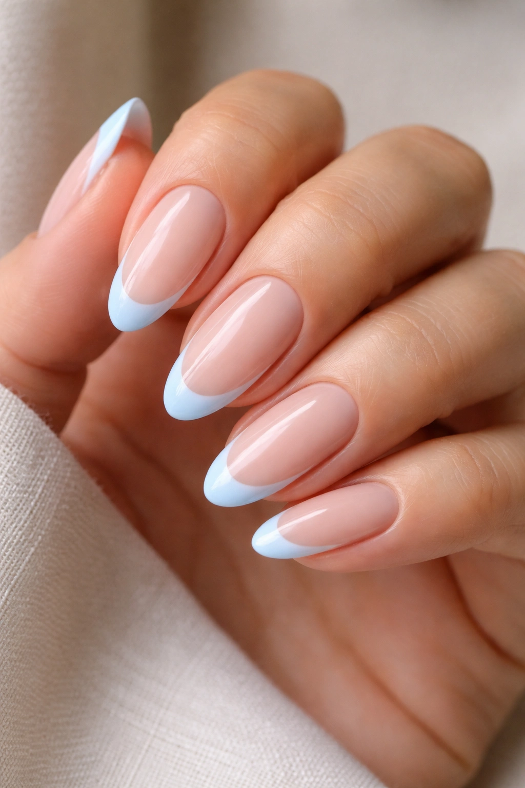 Close-up of nude almond nails with pastel blue French tips