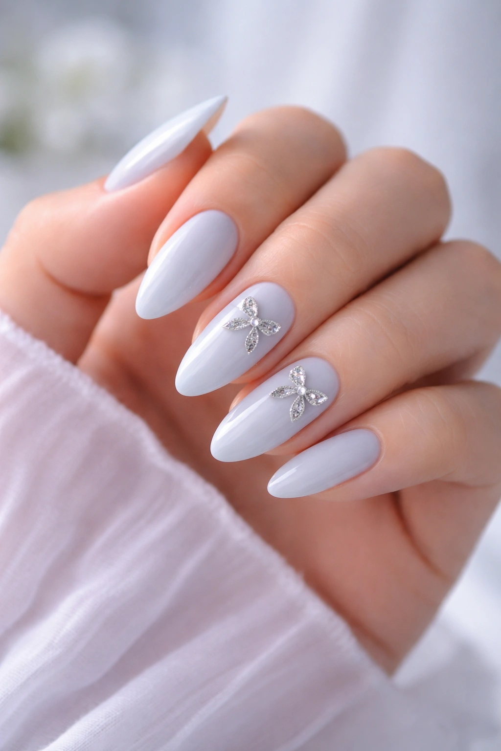 Almond nails in pastel blue with silver ribbon bows on accent nails in a clean studio setting.