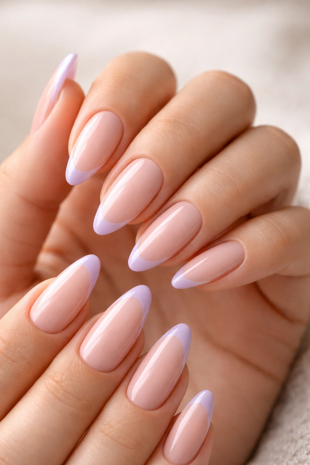 Close-up of hands with pastel tip almond nails featuring sheer base and lavender tips.