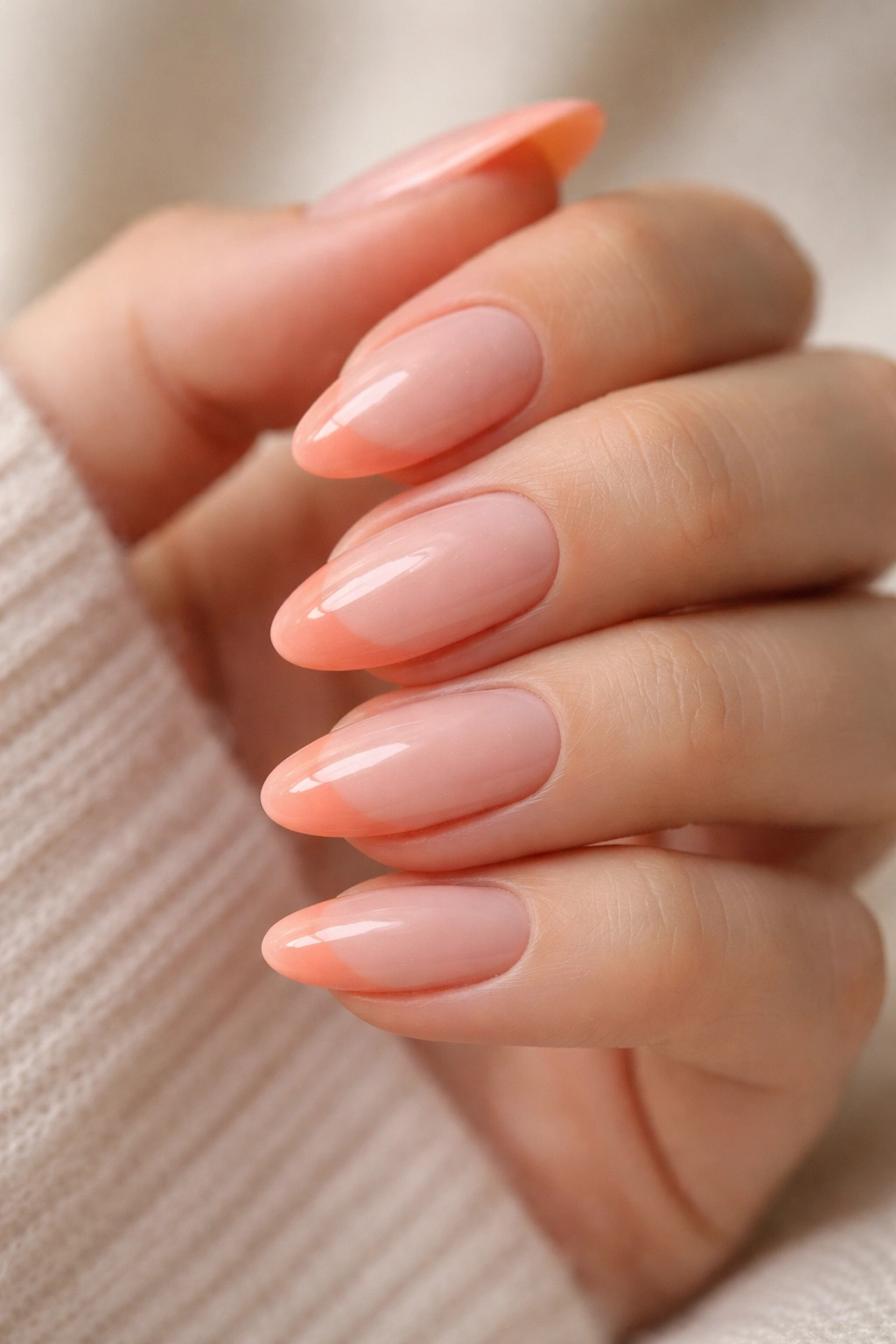 Close-up of almond nails with peach coral French tips on a sheer pink base.