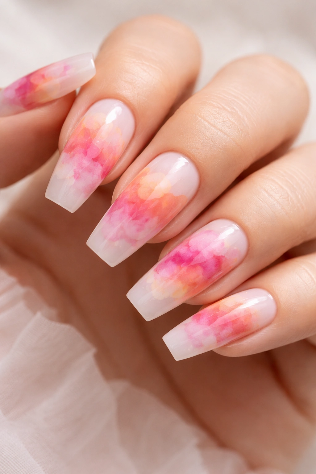 Close-up of coffin nails with peach-to-fuchsia watercolor cloud design on a milky base