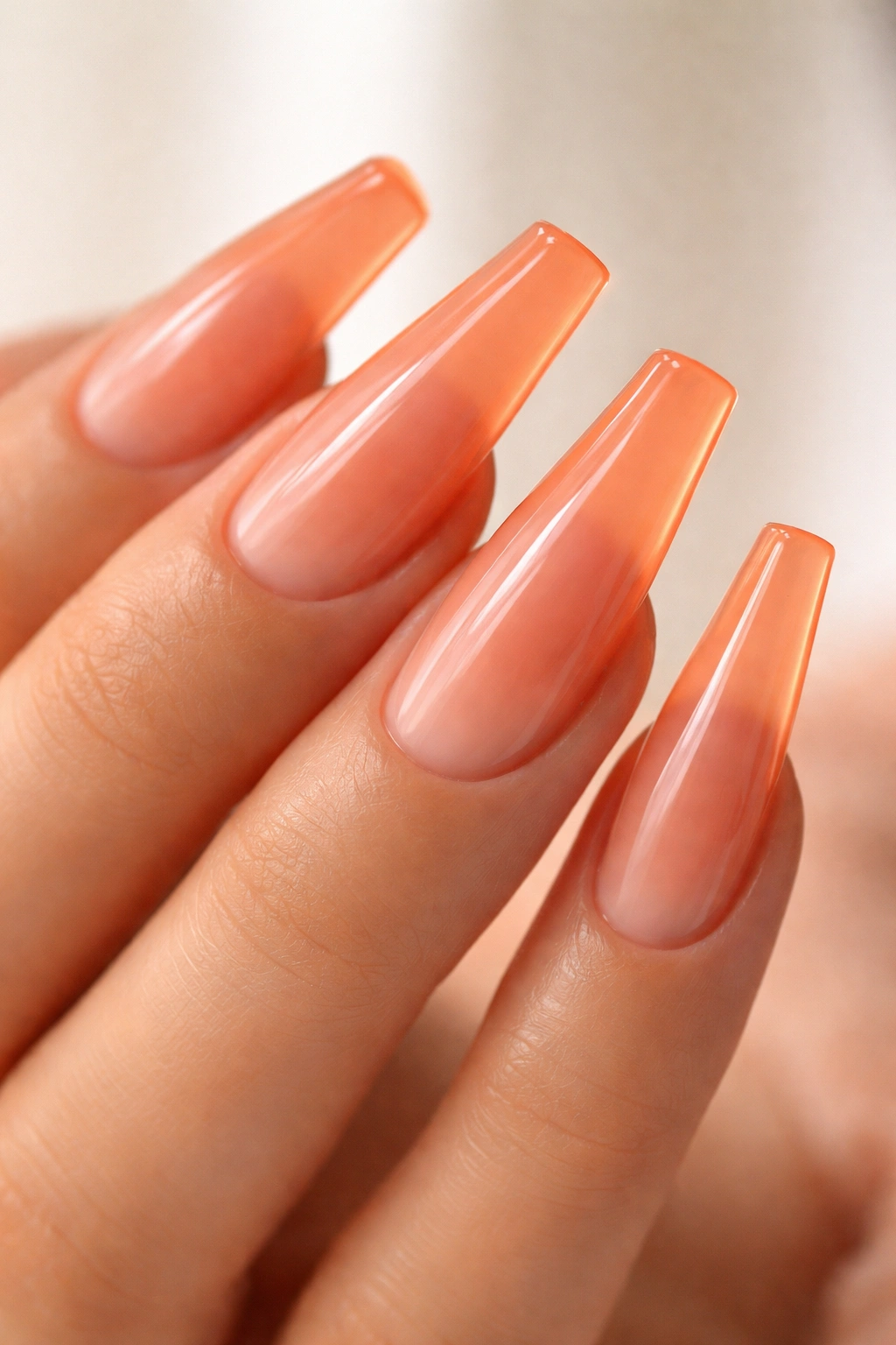 Close-up of peach-orange jelly coffin nails showing translucent glow