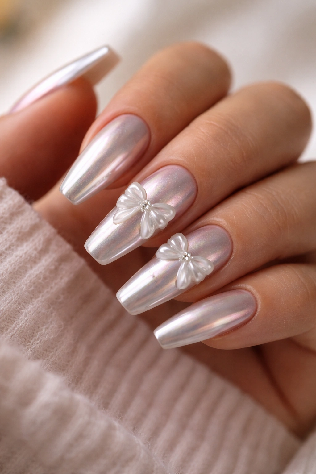 Pearl chrome coffin nails with raised gel bows on a hand