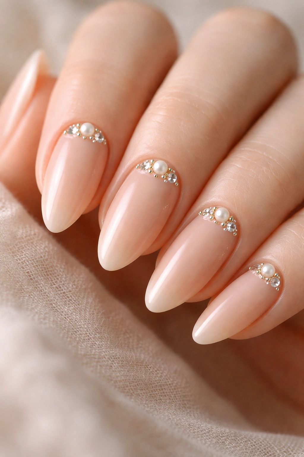 Close-up of almond nails with pearl and crystal accents on nude base