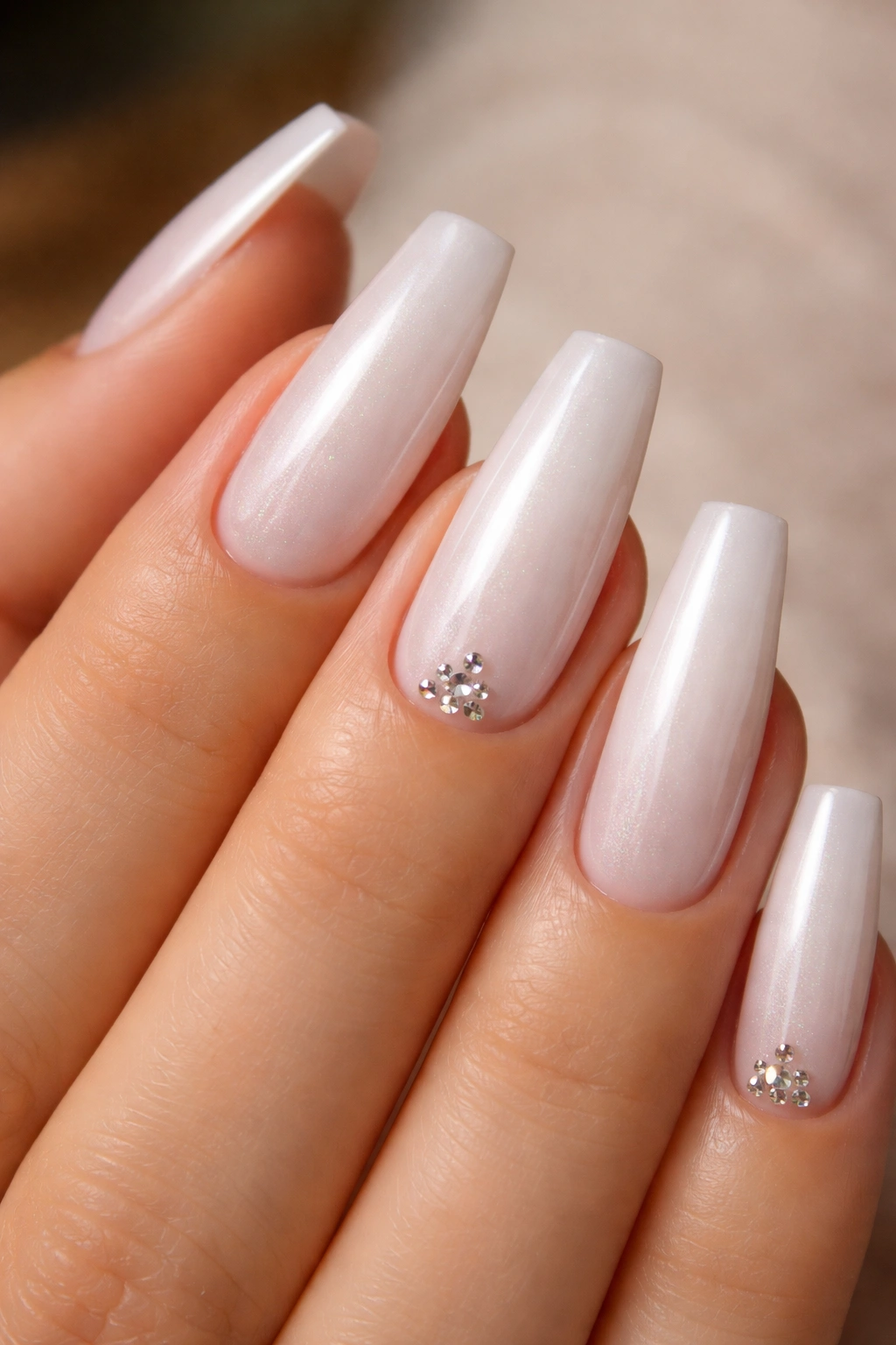 Pearl white coffin nails with tiny crystals near the cuticle on a neutral background