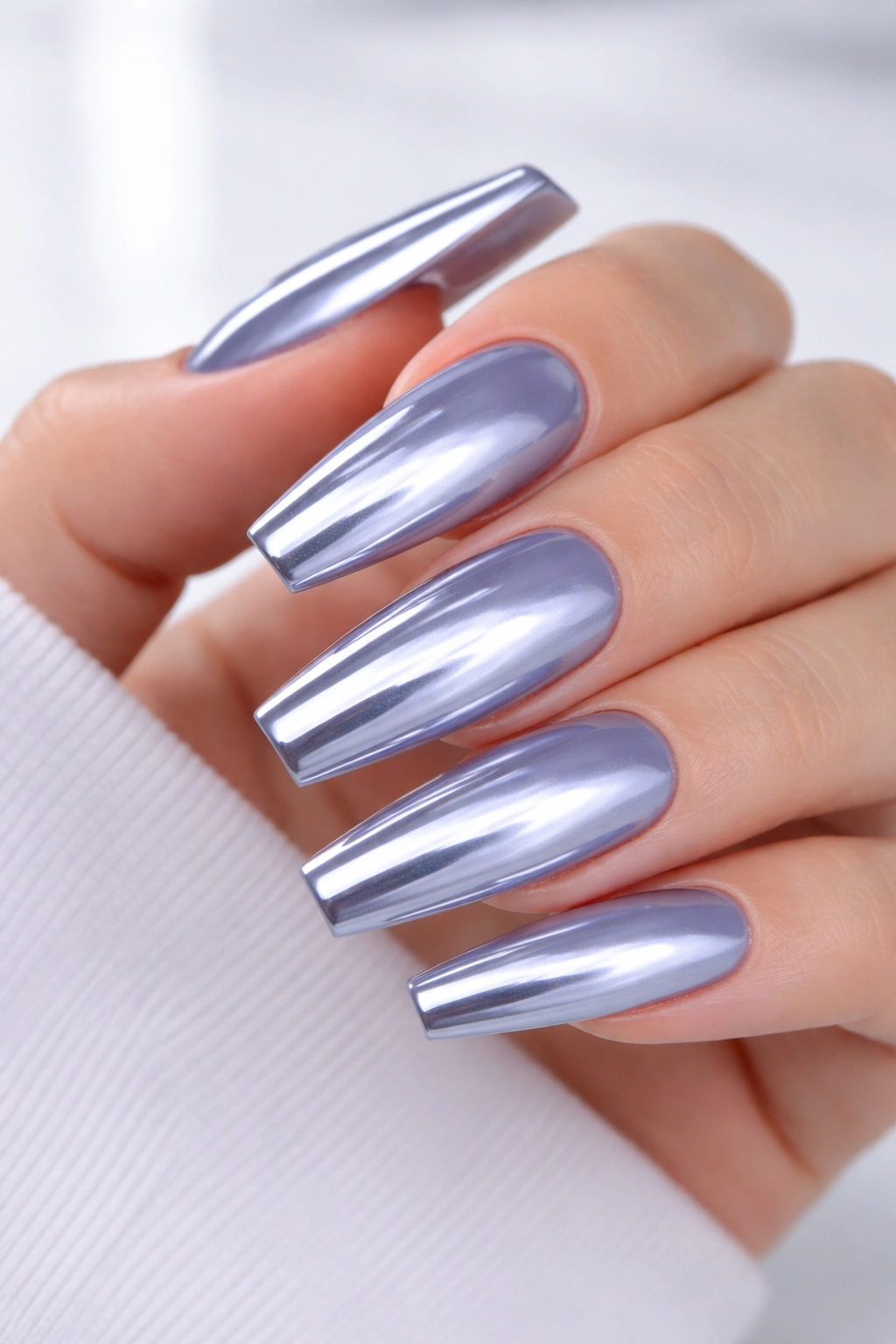 Close-up of icy periwinkle coffin nails with a chrome reflective finish on a hand.
