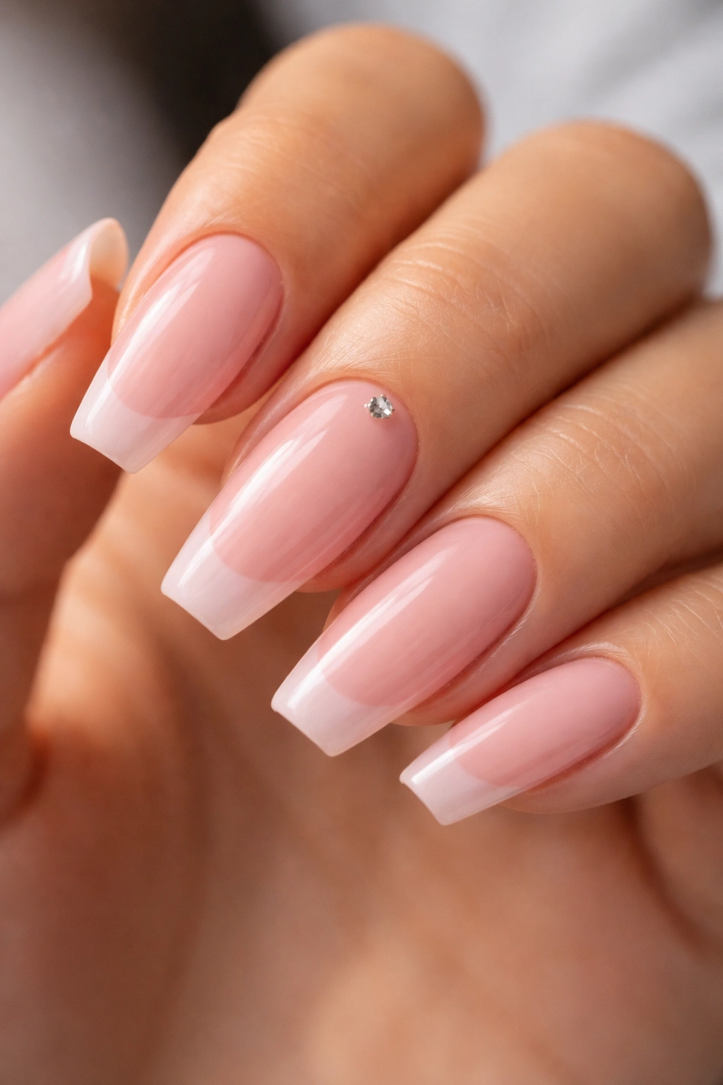Close-up of coffin nails with petal pink French and a single crystal