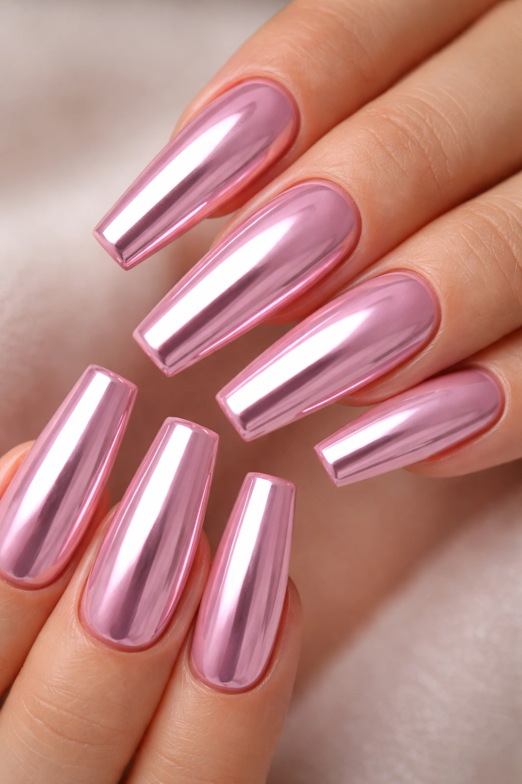 Close-up of baby pink coffin nails with mirror chrome finish on a hand, smooth glossy surface