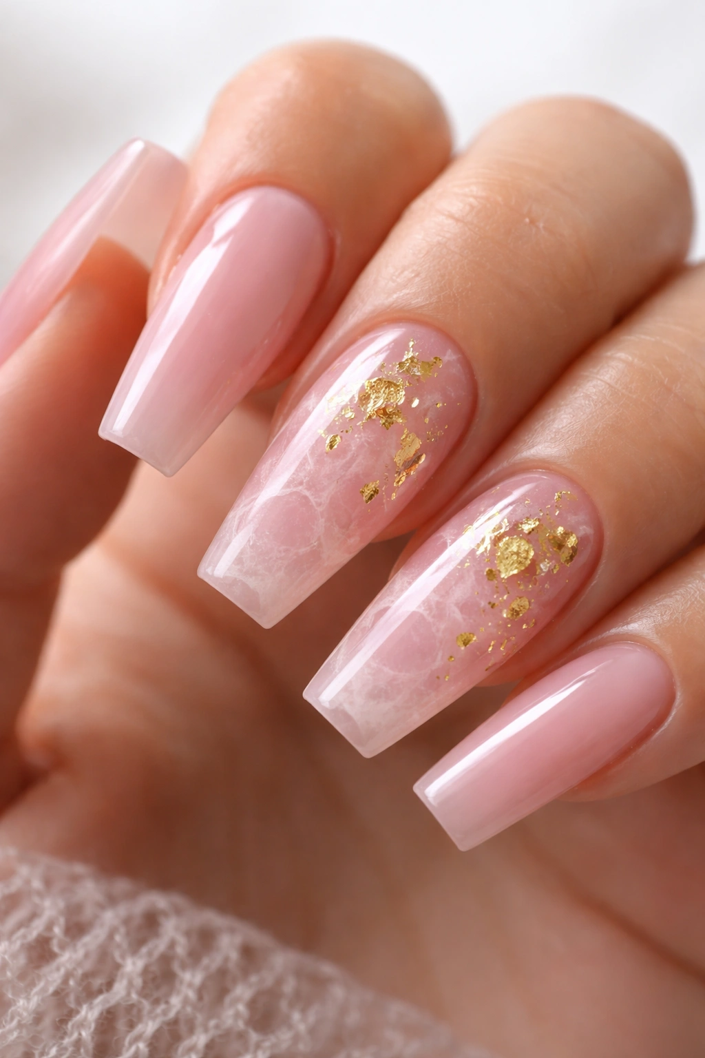Pink quartz nails with white wisps and scattered gold leaf on two nails