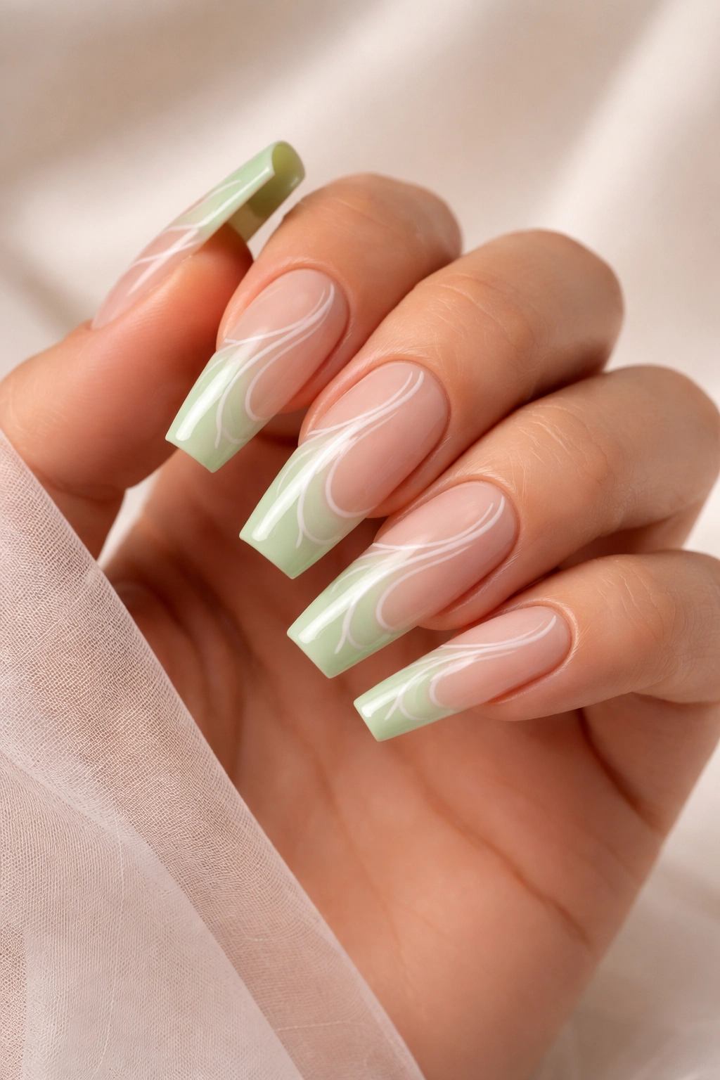 Close-up of pistachio green coffin nails with white swirl linework on a sheer base