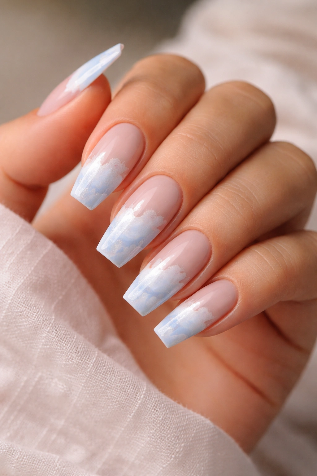 Close-up coffin nails with powder blue cloud art on milky nude base