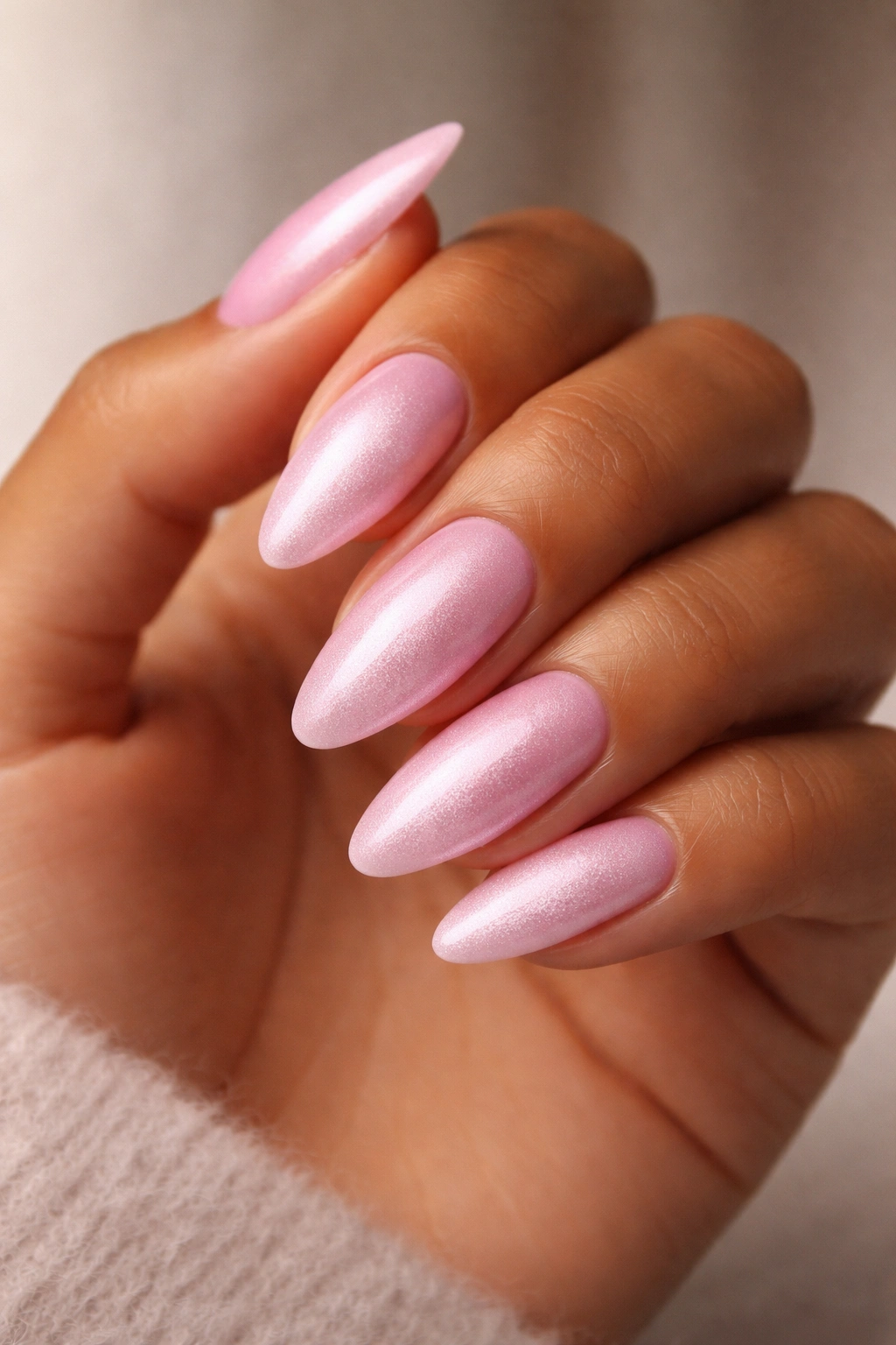 Close-up of powder pink almond nails with velvet finish on a neutral background
