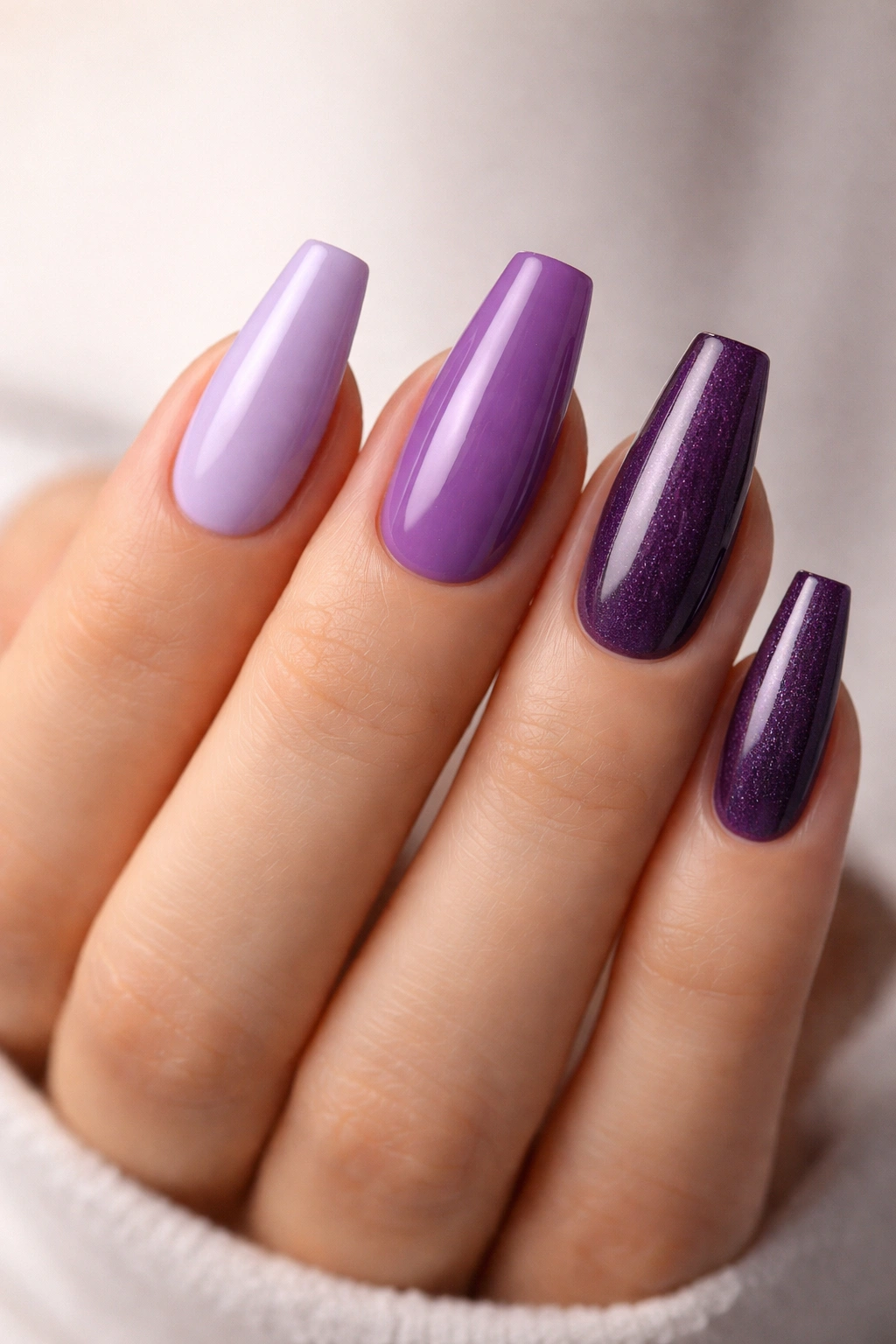 Close-up of a hand with purple coffin nails in varying lengths and undertones to illustrate fit