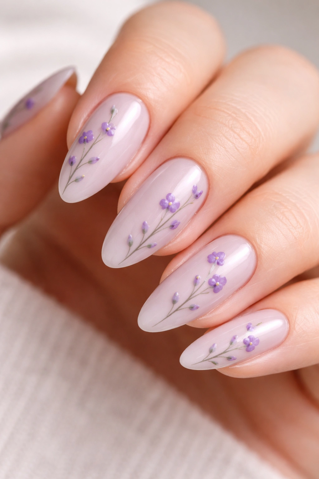 Close-up of almond nails with tiny purple flowers and fine line stems along the side