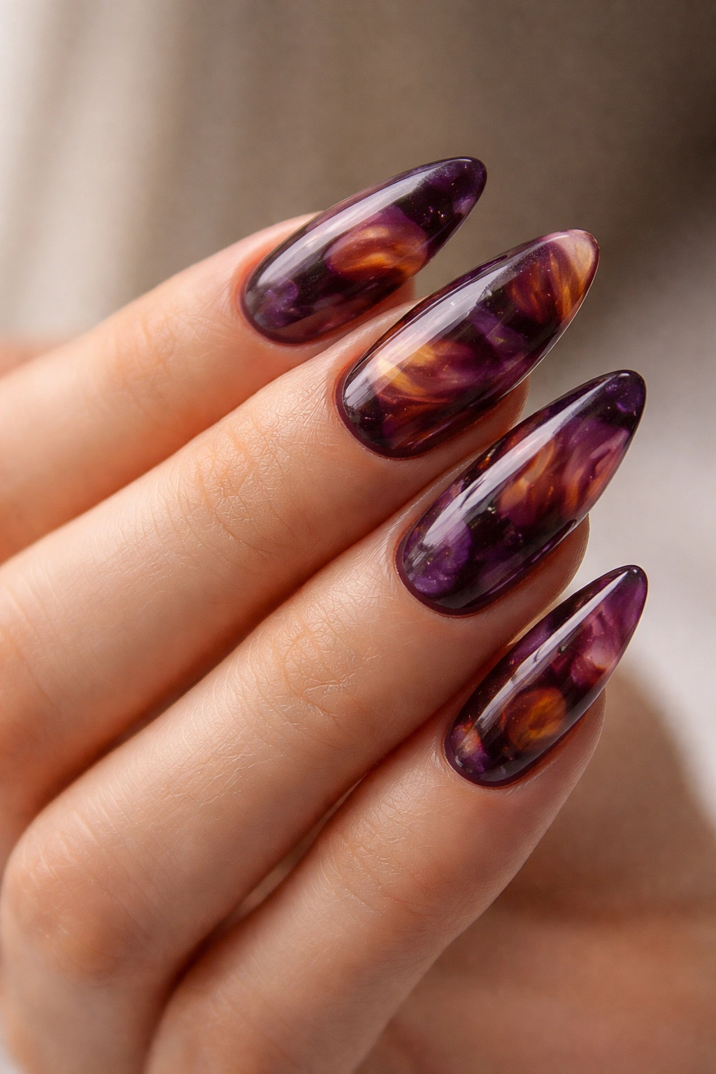 Close-up of purple tortoiseshell almond nails with swirled jelly patches in plum and amber.