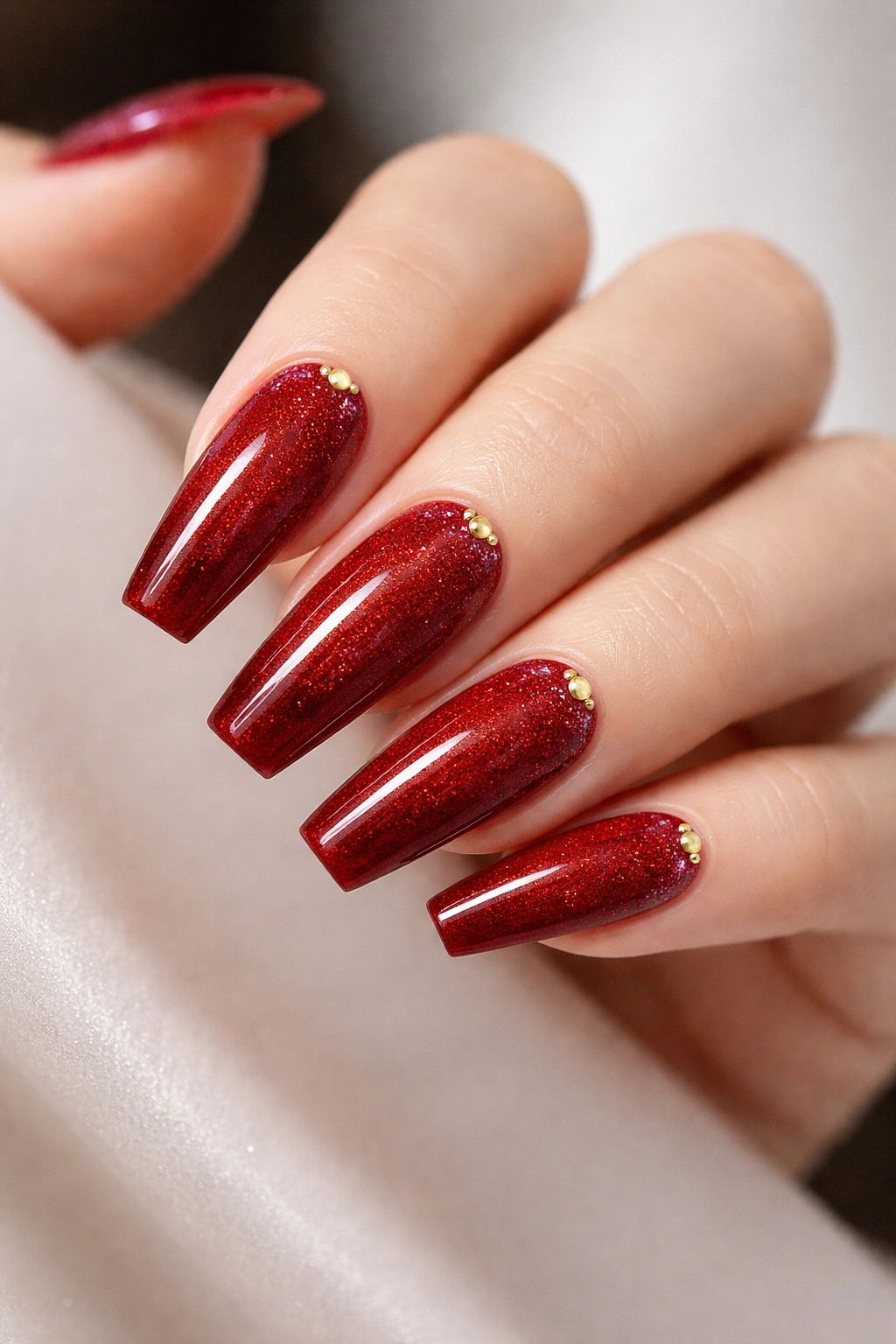 Close-up of coffin nails with cherry red micro glitter fade and gold studs at outer corners