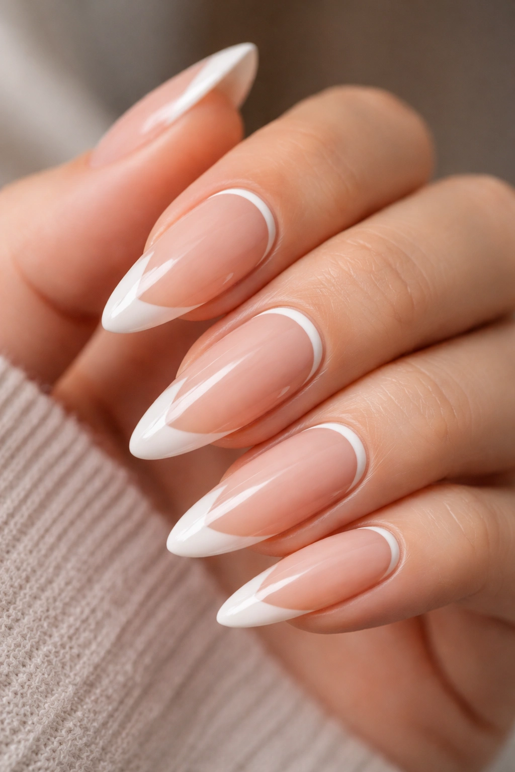 Close-up of long almond nails with a small crescent at the base near the cuticle on a nude base.