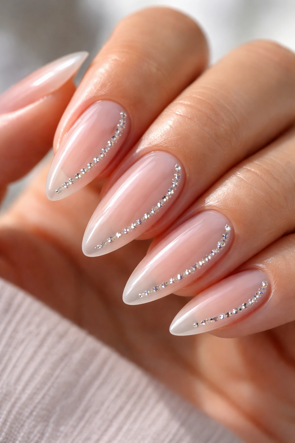 Close-up of almond nails with a clear base and a curved rhinestone trail along the side