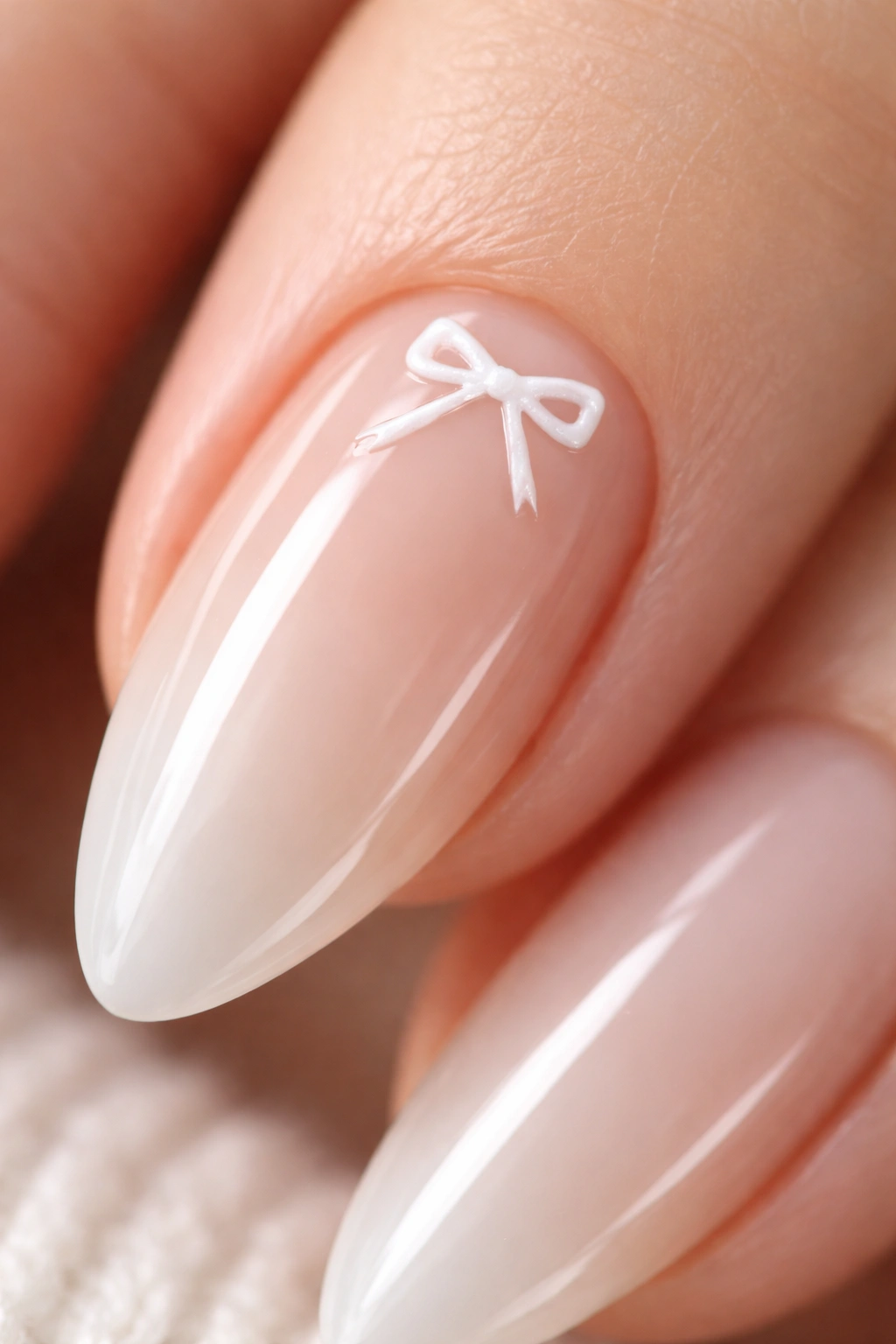 Close-up of an almond nail featuring a tiny white ribbon bow on a sheer nude base
