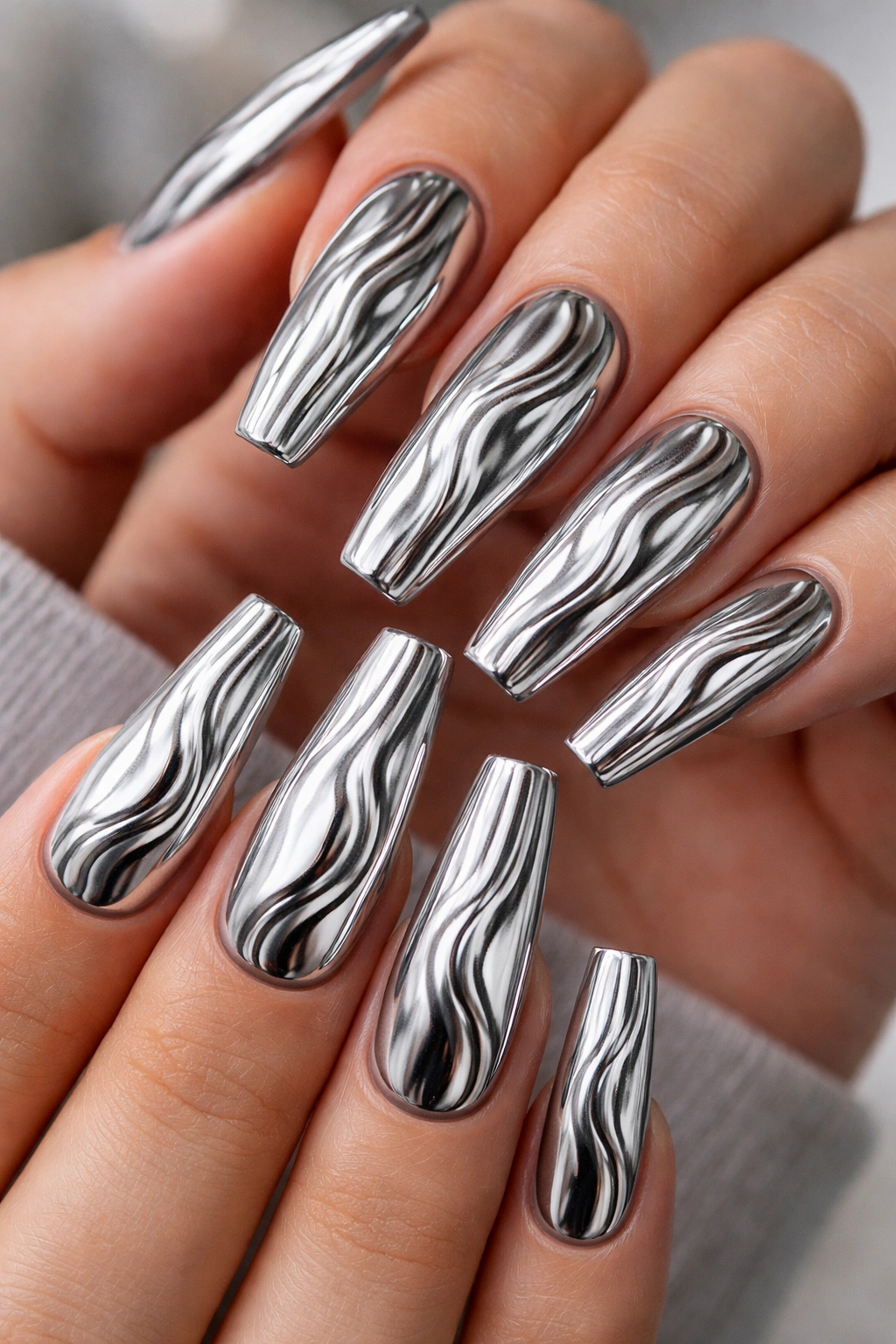 Close-up of long coffin nails with liquid metal ripple silver chrome finish and raised ridges catching light