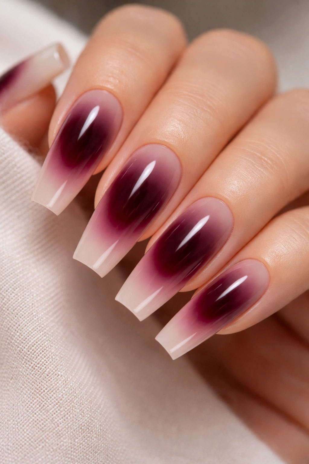 Close-up of rosy nude coffin nails with dark cherry aura centers and soft glow