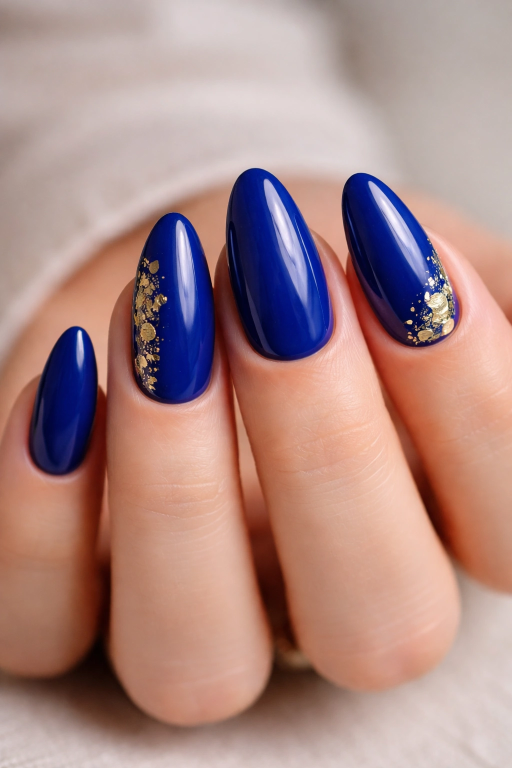Close-up of almond nails in royal blue with gold foil flakes