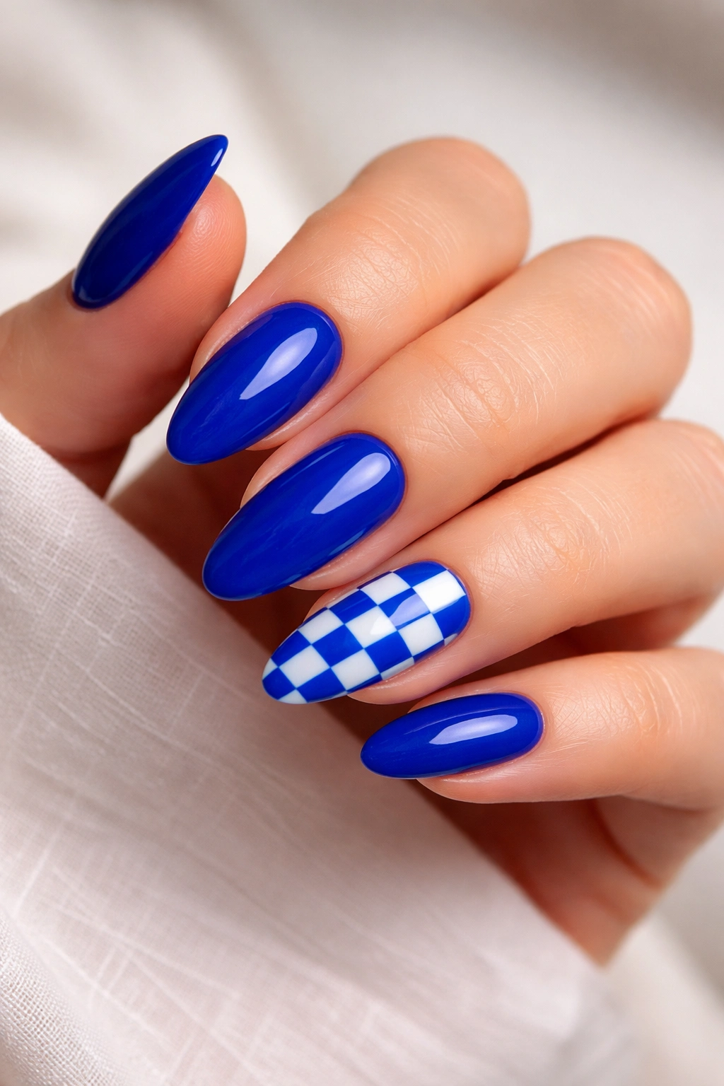 Close-up of almond nails with a royal blue checkerboard accent on one nail