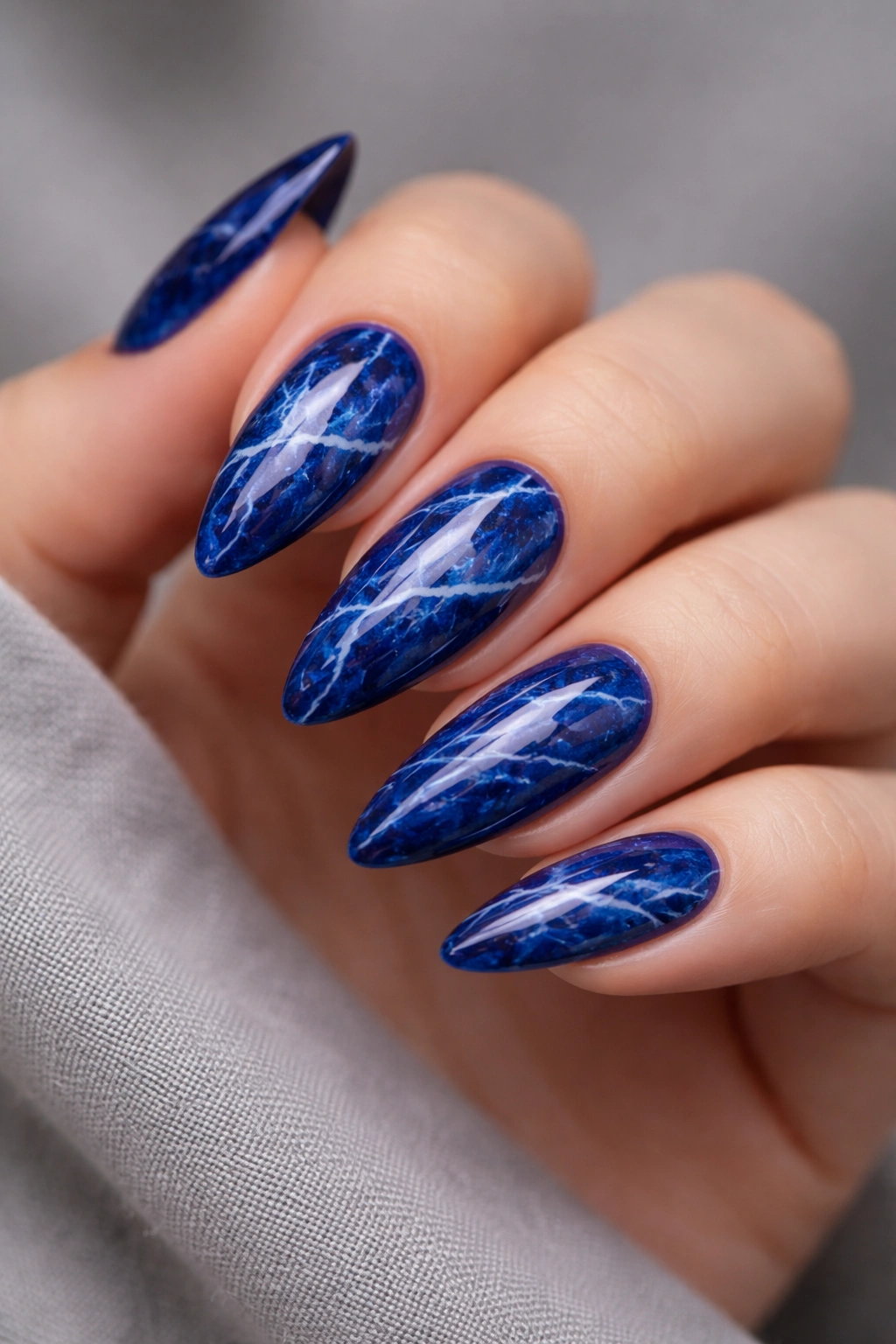 Almond nails with royal blue marble and delicate white veins on a neutral background