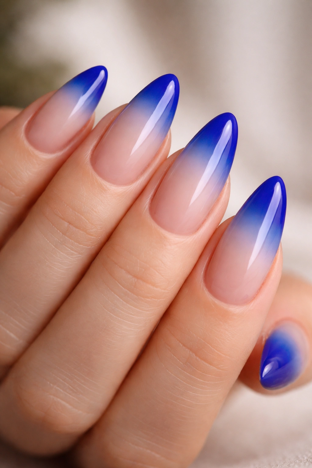 Almond nails with nude-to-blue ombré fade on royal blue base