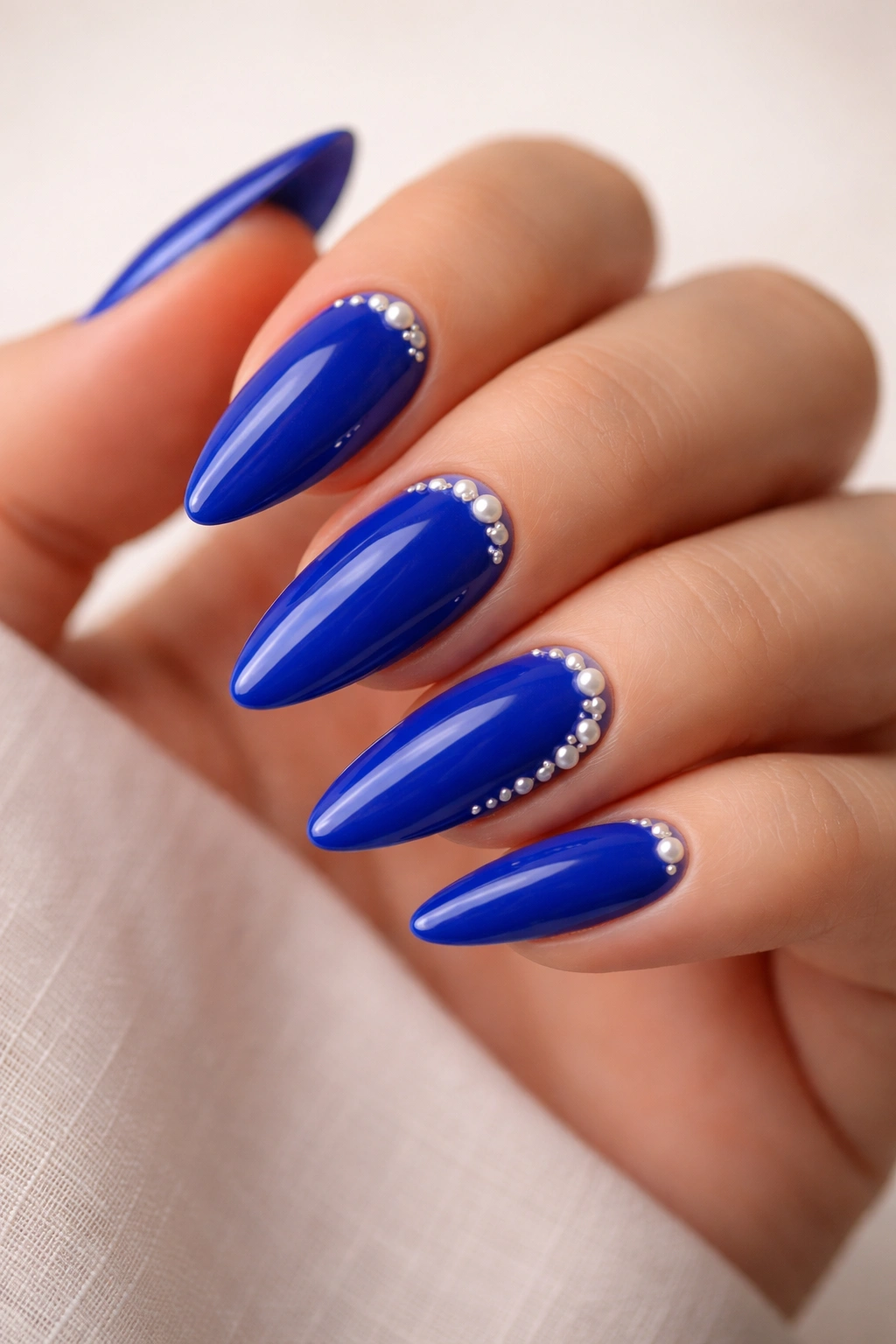 Royal blue almond nails with small pearl accents near cuticle