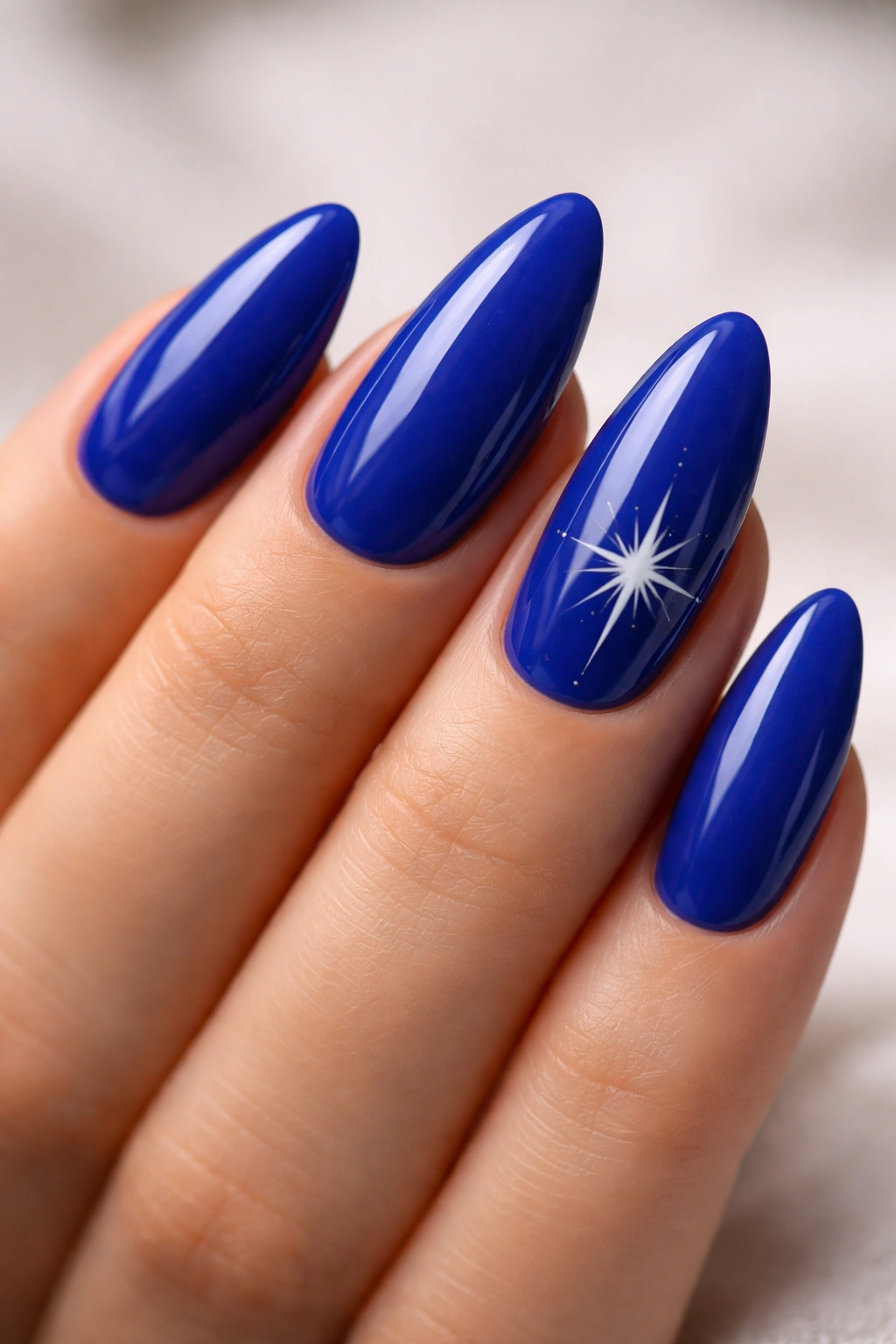Royal blue almond nails with a white starburst accent on one nail