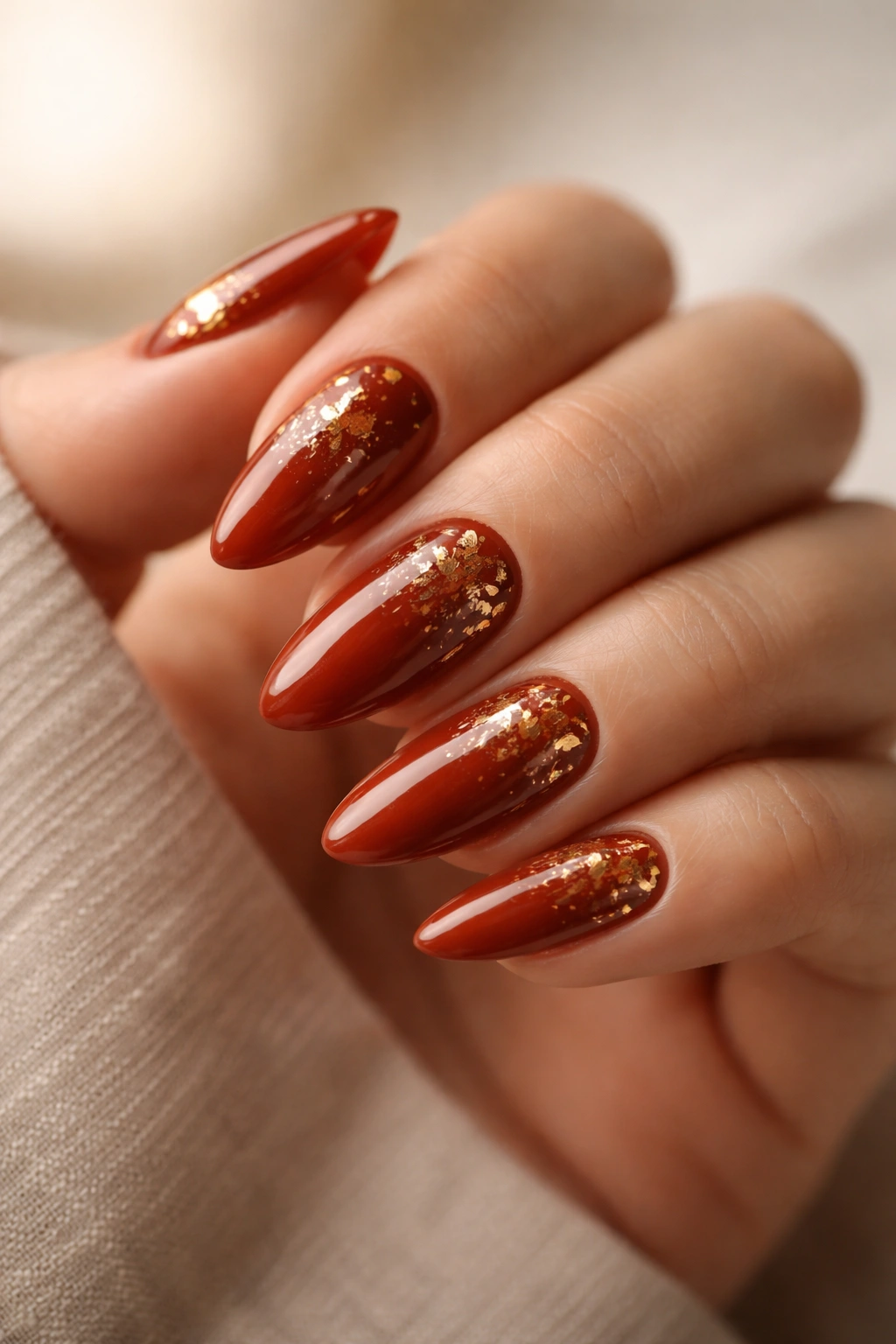 Close-up of almond nails with rust base and gold foil accents