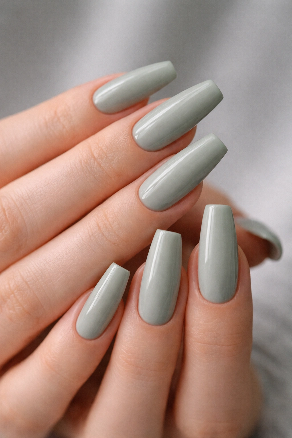 Close-up of sage green coffin nails with a glossy finish on hands